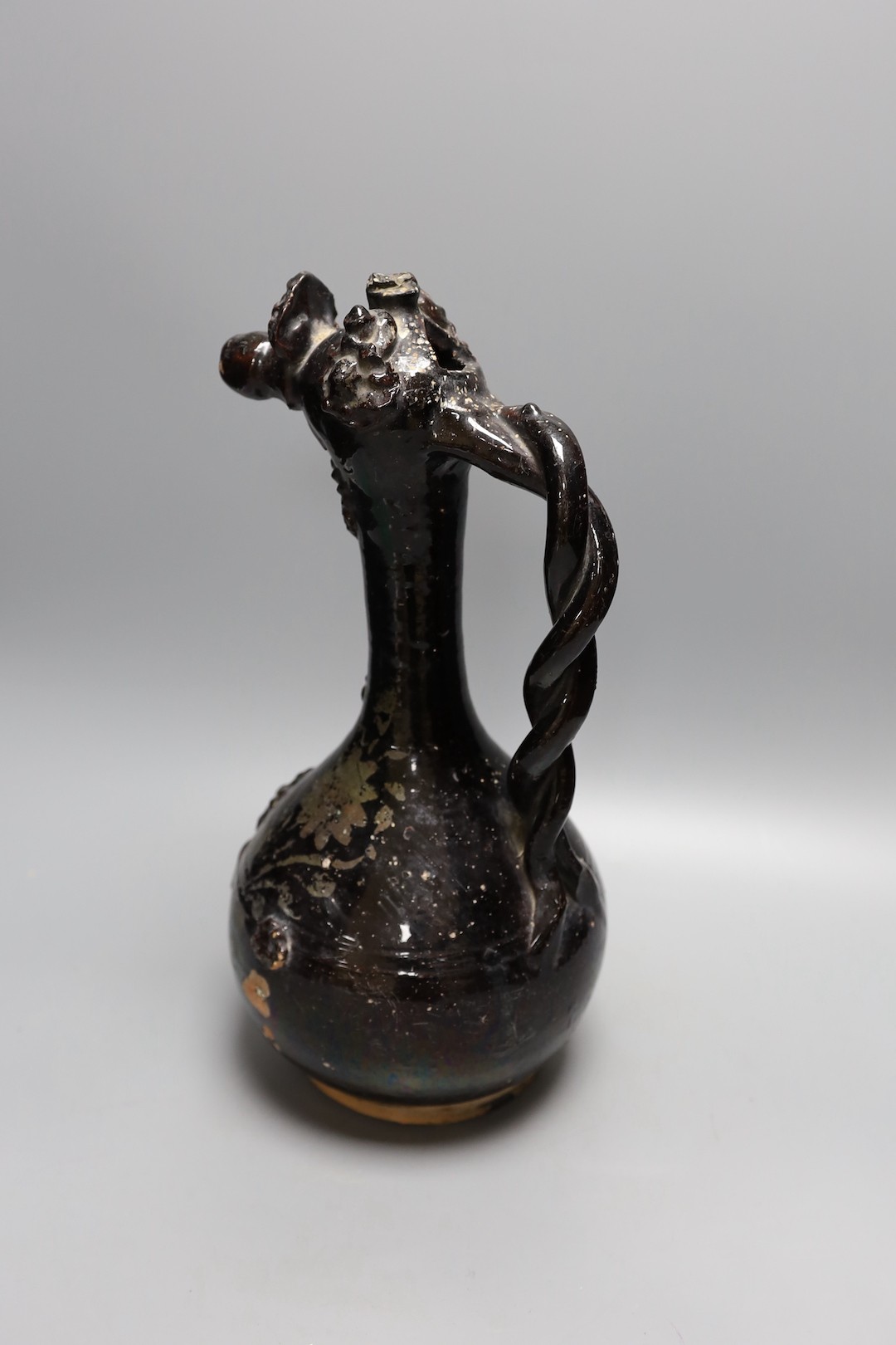 A primitive black glazed terracotta ewer with decorative headed spout and twisted handle - 38cm high